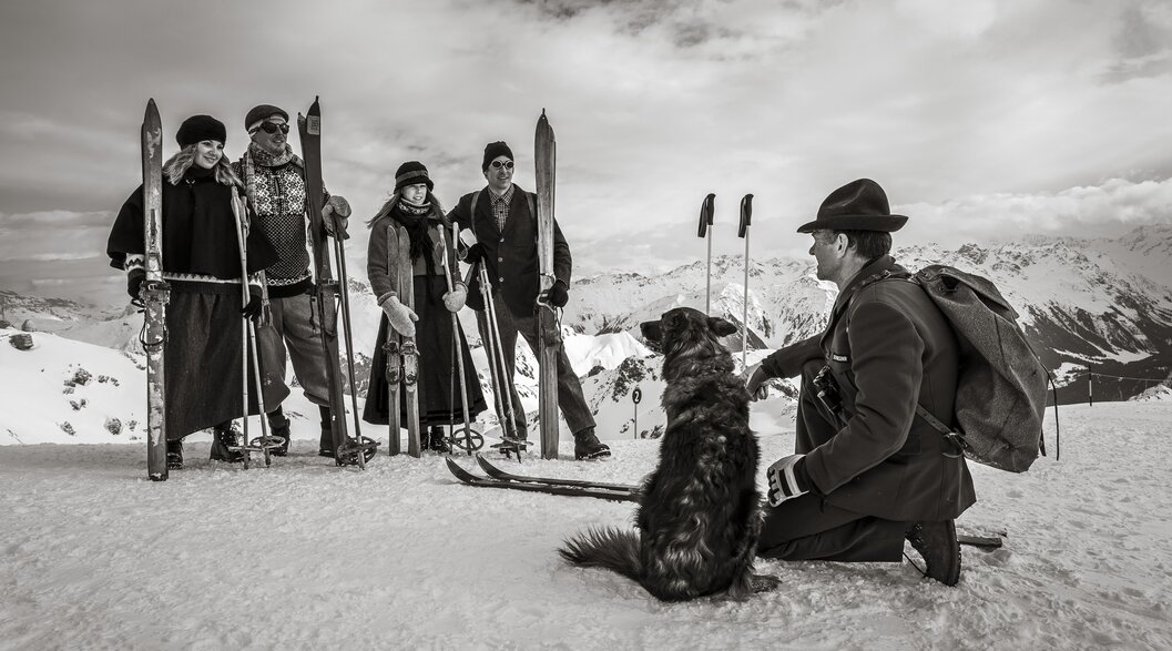 Eine Gruppe Skifahrer nostalgisch gekleidet hört dem Rettungschef mit Hund zu.  | © Davos Klosters Mountains