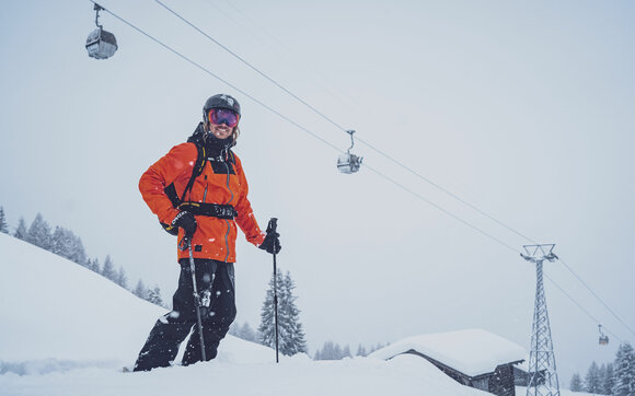 The skier stands happily in the deep snow, the gondolas of the Rinerhorn behind him. | © Davos Klosters Mountains