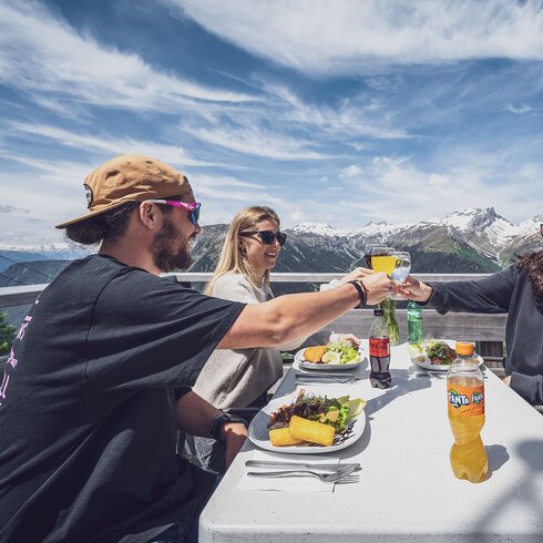 Drei Freunde stossen an und freuen sich auf Ihr Mittagessen auf der Sonnenterrasse Jatzmeder. | © Davos Klosters Mountains