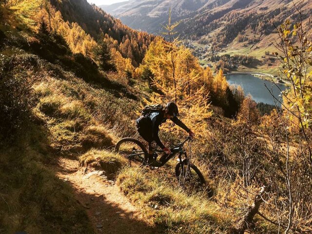Biker fährt in herbstlicher Stimmung auf dem Drusatscha Trail, im Hintergrund der Davoser See.  | © Matteo Manno