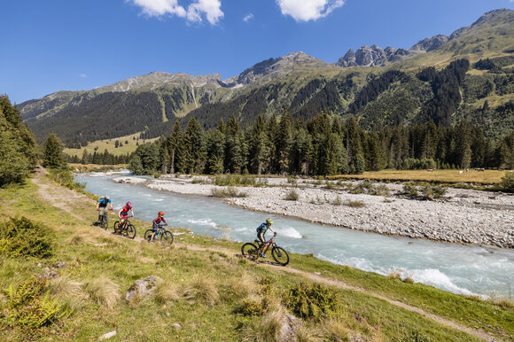 Eine Familie mit zwei grösseren Kindern fährt der Landquart entlang in Richtung Alp Garfiun.  | © Destination Davos Klosters | Martin Bissig