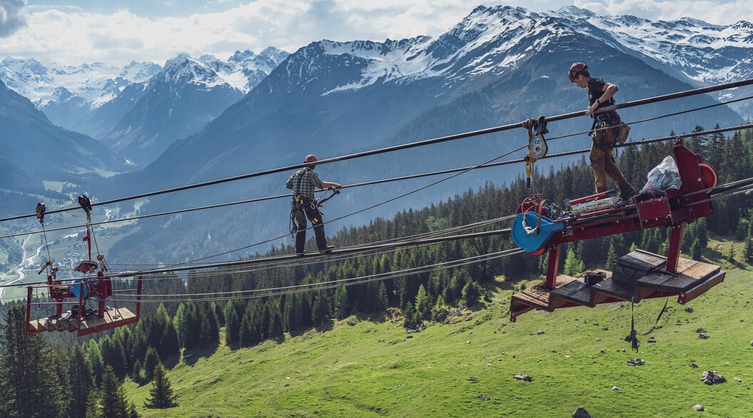 Zwei Arbeiter auf dem Seil der Gotschnabahn | © Davos Klosters Mountains Zwei Arbeiter klettern auf dem Tragseil zur sogenannten Melkmaschine. | © Davos Klosters Mountains
