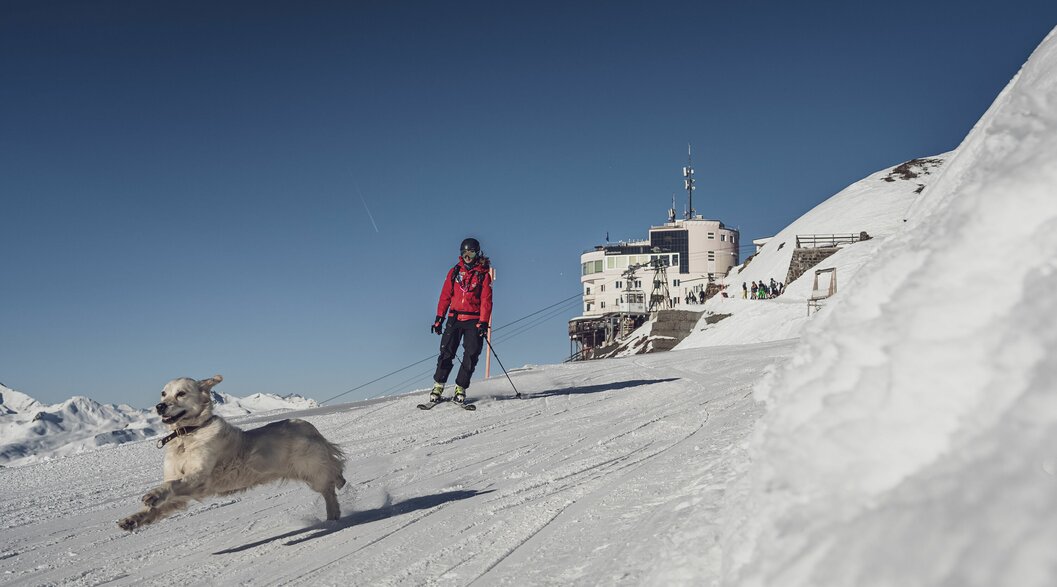 Patrouilleurin mit Hund Jakobshorn | © Davos Klosters Mountains Patrouilleurin Seraina fährt mit ihren Skiern von der Bergstation Jakobshorn weg, begleitet von Hündin Emma. | © Davos Klosters Mountains