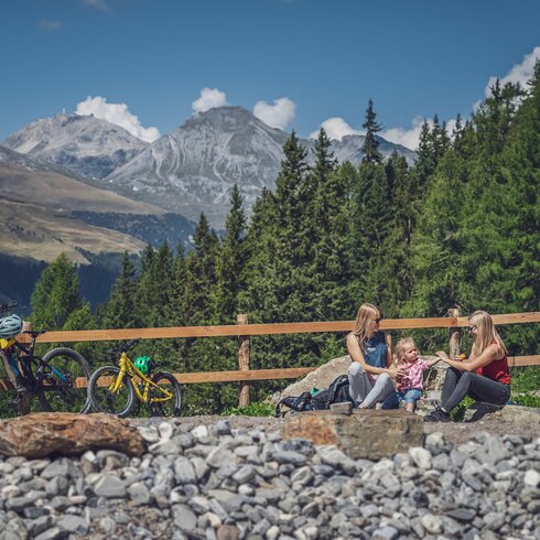 Zwei Frauen und ein Mädchen sitzen am Ufer eines Bergsees, daneben steht ein grosses und ein kleines Bike. | © Davos Klosters Mountains