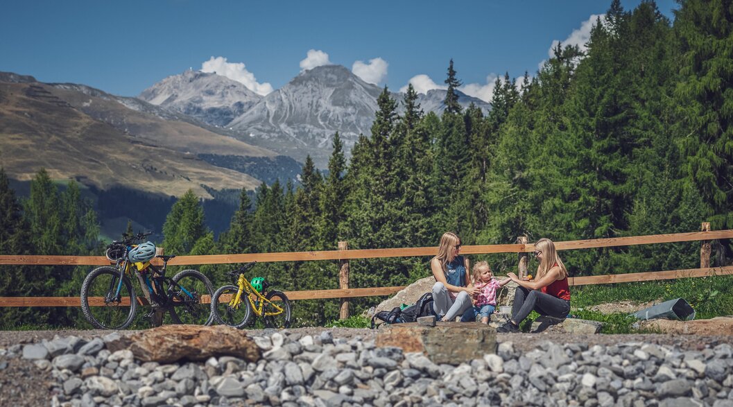 Zwei Frauen und ein Mädchen sitzen am Ufer eines Bergsees, daneben steht ein grosses und ein kleines Bike. | © Davos Klosters Mountains