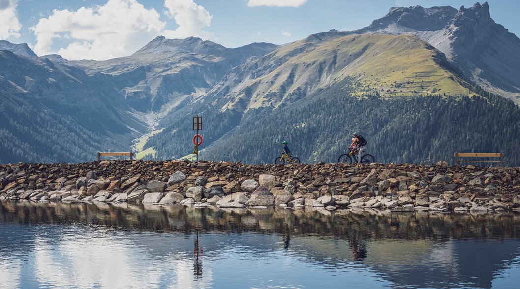 Eine Frau fährt mit ihren beiden Kindern mit dem Mountainbike am Seeufer entlang. | © Davos Klosters Mountains