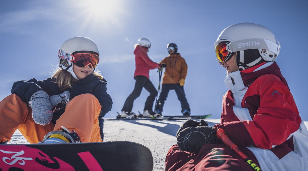 Familientag am Rinerhorn | © Davos Klosters Mountains Zwei Mädchen mit ihren Eltern im Hintergrund machen eine Pause auf der Piste. | © Davos Klosters Mountains
