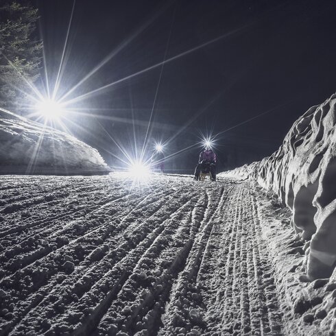 Mädchen mit Taschenlampe schlittelt auf der Nachtpiste hinunter. | © Davos Klosters Mountains