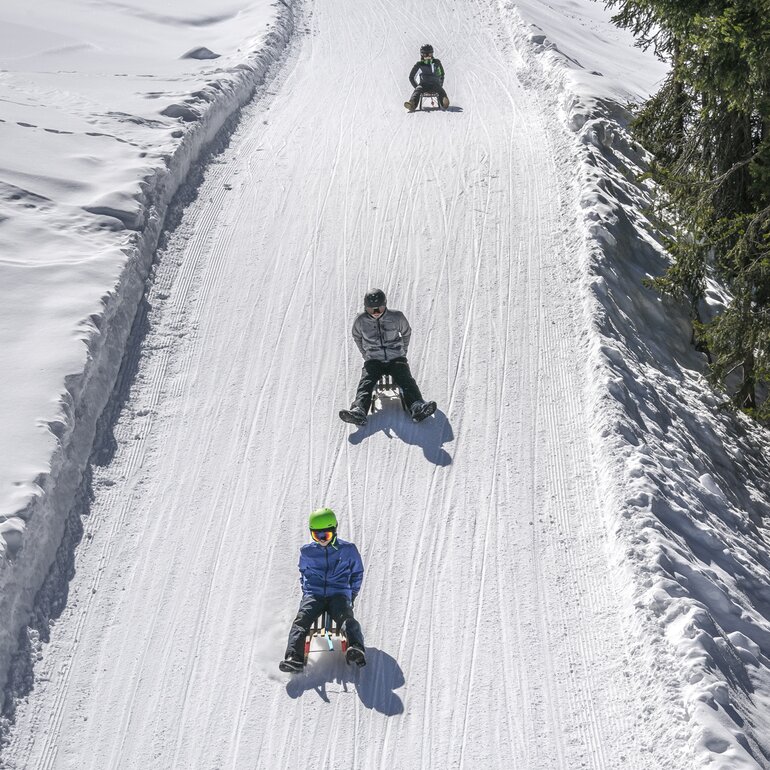 Group of young guys on sledge whiz down the prepared sled run. | © Davos Klosters Mountains