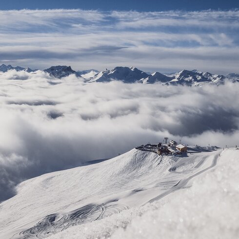 Aufnahme aus der Ferne mit Sicht auf die Jatzhütte Davos welche über den Wolken ersichtlich ist. | © Davos Klosters Mountain