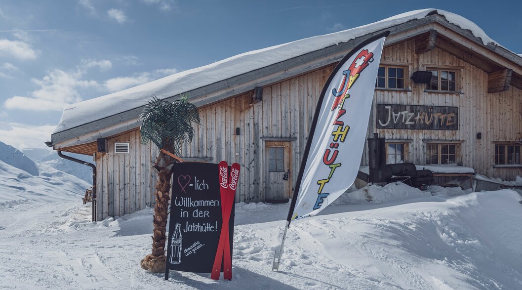 Willkommen Jatzhütte Jakobshorn | © Davos Klosters Mountains Jatzhütte auf dem Jakobshorn mit Willkommens-Schild und Fahne vor der Hütte. | © Davos Klosters Mountains