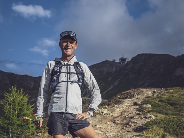 Trailrunning Trainer Guy Nunige | © Davos Klosters Mountains Guy Nunige steht auf dem Vertical Run Jakobshorn und blickt in die Kamera, hinter ihm liegt die Bergstation Jakobshorn. | © Davos Klosters Mountains