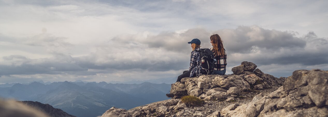 Wanderfreundinnen bei einer Pause | © Davos Klosters Moutains Wanderfreundinnen geniessen die Aussicht auf einem Stein. | © Davos Klosters Moutains