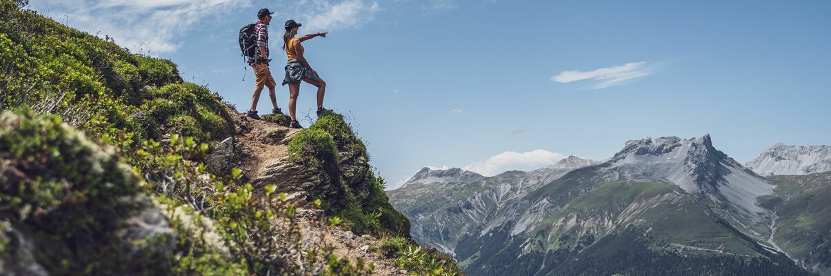 Mann und Frau stehend auf einem Felsen, sie schauen in die Ferne  | © Davos Klosters Mountains 