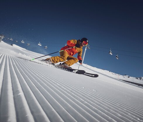 Ein Skifahrer am carven vor der Liftanlage auf einer perfekt präparierten Piste in der Sonne | © Davos Klosters Bergbahnen AG