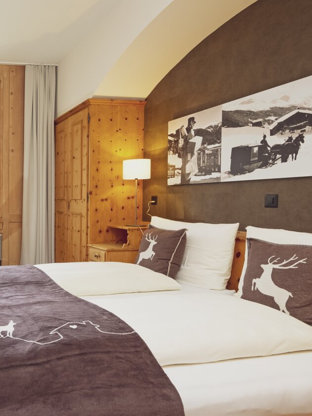 Doppelbettzimmer mit Bettwäsche im Hirschstyle, Fenster mit Stuhl und Holzeinrichtung | © Davos Klosters Mountains 
