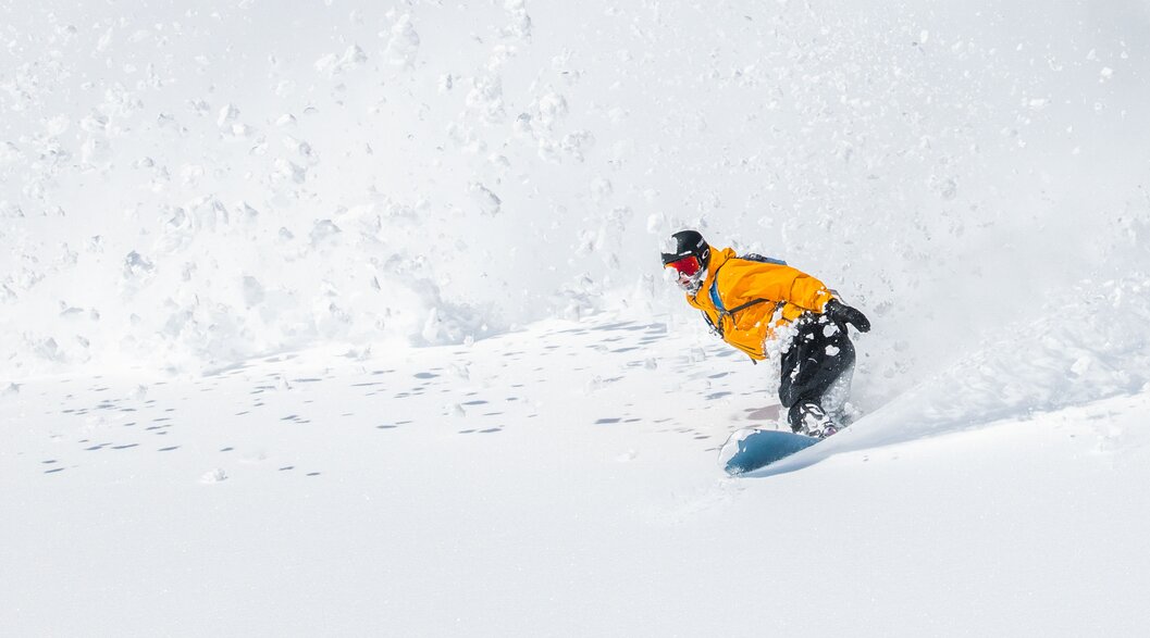 Snowboardfahrer gleitet fröhlich einen schneebedeckten Hang hinunter und hinterlässt frische Spuren im Schnee | © Laax